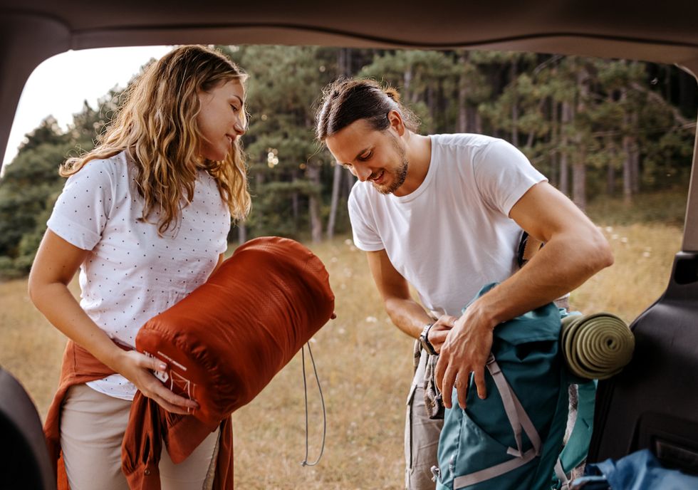 smiling young couple, packing up camping equipment in the trunk of a car, ready for walking