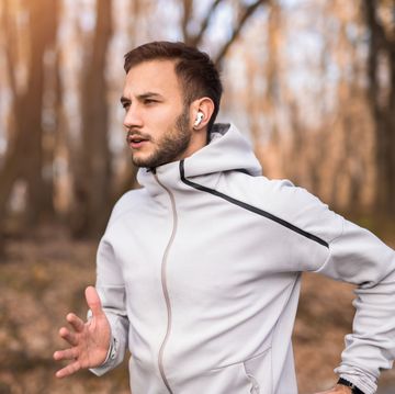 close up of athletic young man running outdoors and listening to music on wireless headphones