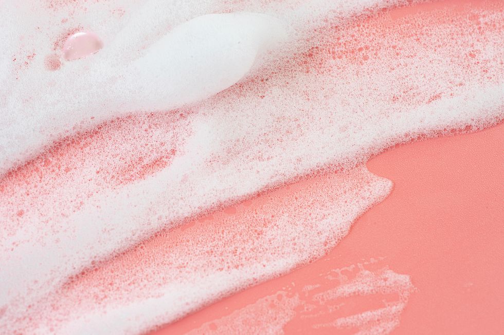 smears of white foam soap or cosmetic milk or beauty foam on pastel pink coral rose color background texture of white foam concept of home facial cleanser in selfcare routine and healthy lifestyle flat lay close up copy space