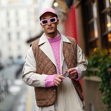 street style hombre con chaleco, gabardina, gafas de sol y gorra rosas