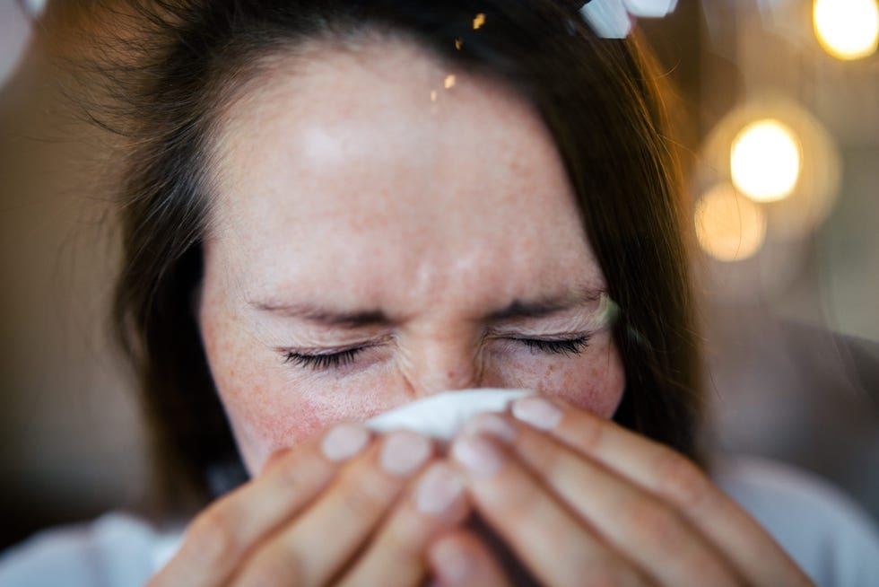 woman sneezing behind a window, using a tissue.