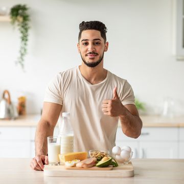 portrait of handsome fit young arab man offering healthy products rich in protein and showing thumb up gesture at kitchen middle eastern guy recommending wholesome nutrition at home