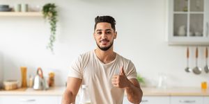 portrait of handsome fit young arab man offering healthy products rich in protein and showing thumb up gesture at kitchen middle eastern guy recommending wholesome nutrition at home
