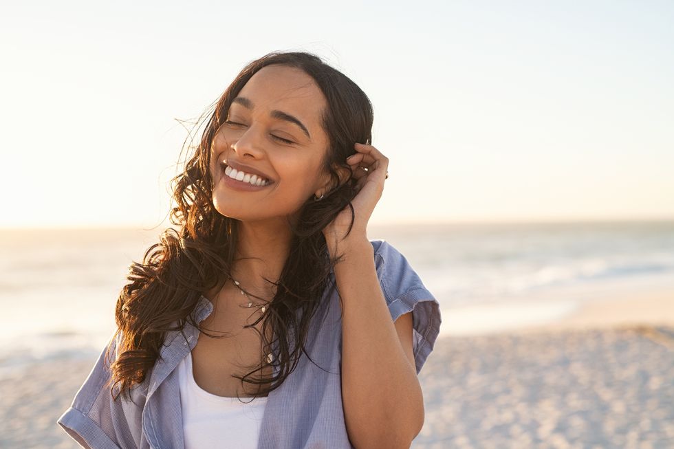 smiling latin hispanic woman relaxing on beach with closed eyes at sunset beautiful mixed race woman enjoying wind fluttering hair charming and calm young woman breathing fresh air at summer beach with copy space