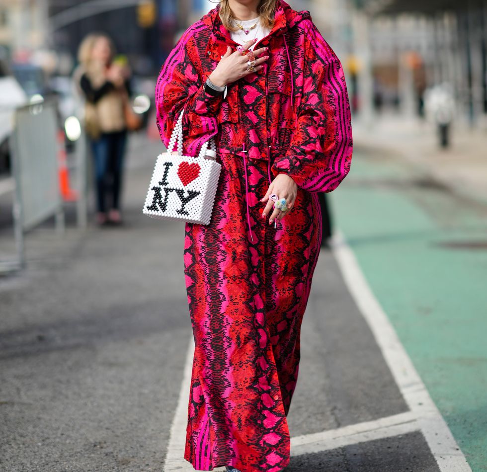 new york, new york february 12 a guest wears a red pink black snake print pattern cap from ivy park, a matching red pink black snake print pattern oversized long coat from ivy park, a large oversized pendant earring, gold large chain pendants necklaces, a white t shirt, large multicolored plastic rings, a white black red pearls "i love ny" print pattern handbag, white leather and fabric sneakers, outside song jun wan, during new york fashion week, on february 12, 2022 in new york city photo by edward berthelotgetty images