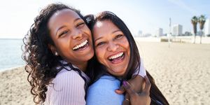 close up photography of multiracial family, looking and smiling at camera, daughter hugging her mother, standing on the beach, woth big smile