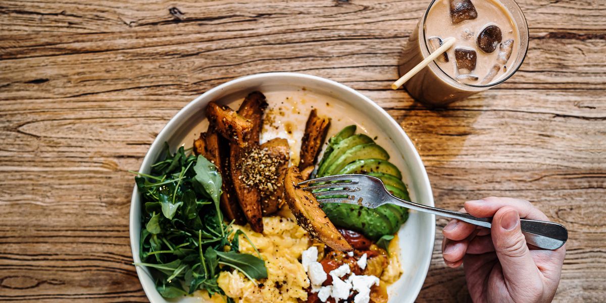 flat lay shot of man having healthy vegan green salad bowl for brunch in cafe table top view of a man eating breakfast with a glass of iced latte sitting at wooden dining table healthy eating lifestyle people, food and lifestyle concept