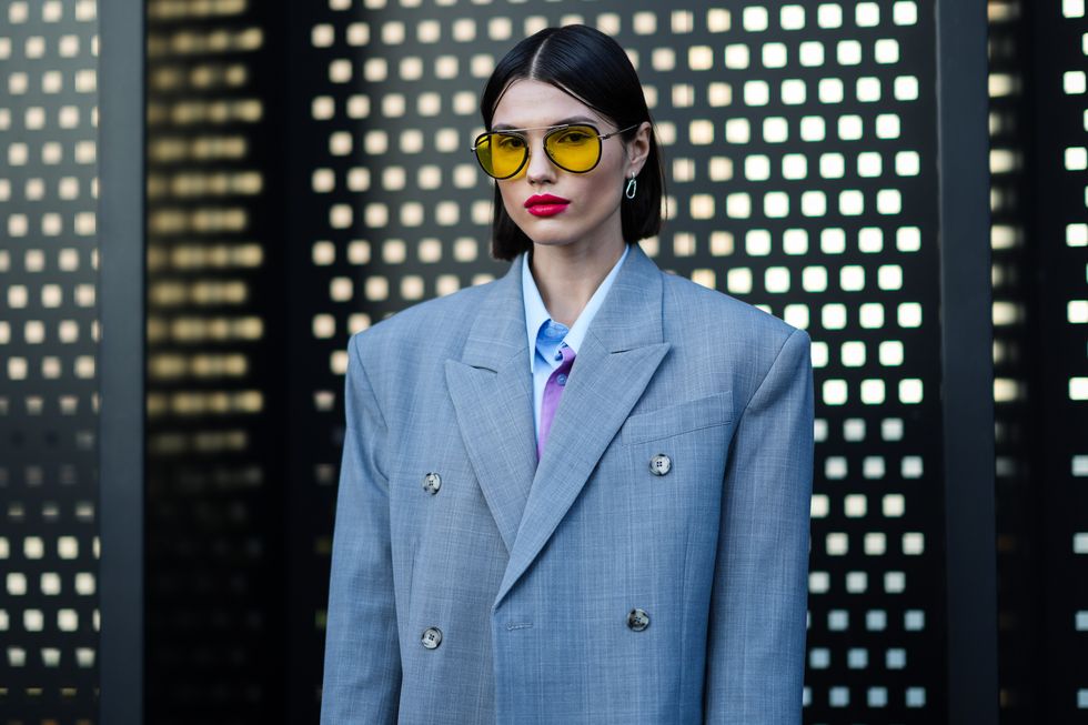 milan, italy   february 25 a guest wears yellow sunglasses, silver earrings, a pale gray oversized blazer jacket with epaulets, a white  baby blue  pale purple oversized shirt, outside the gucci  fashion show, during the milan fashion week fallwinter 20222023 on february 25, 2022 in milan, italy photo by edward berthelotgetty images