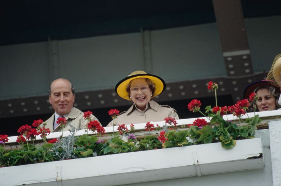 british peer and racing manager to queen elizabeth ii henry herbert, 7th earl of carnarvon 1924 2001 and british royal queen elizabeth ii, wearing a yellow and black hat and a raincoat, watching the epsom derby at epsom downs racecourse on epsom downs, surrey, england, 6th june 1990 photo by tim graham photo library via getty images