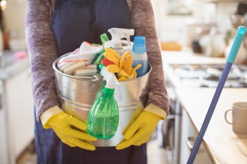 portrait cropped woman holding bucket of cleaning supplies in kitchen, doing chores