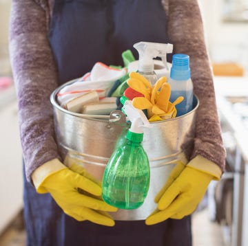 how-often-to-clean-kitchen-essentials portrait cropped woman holding bucket of cleaning supplies in kitchen, doing chores