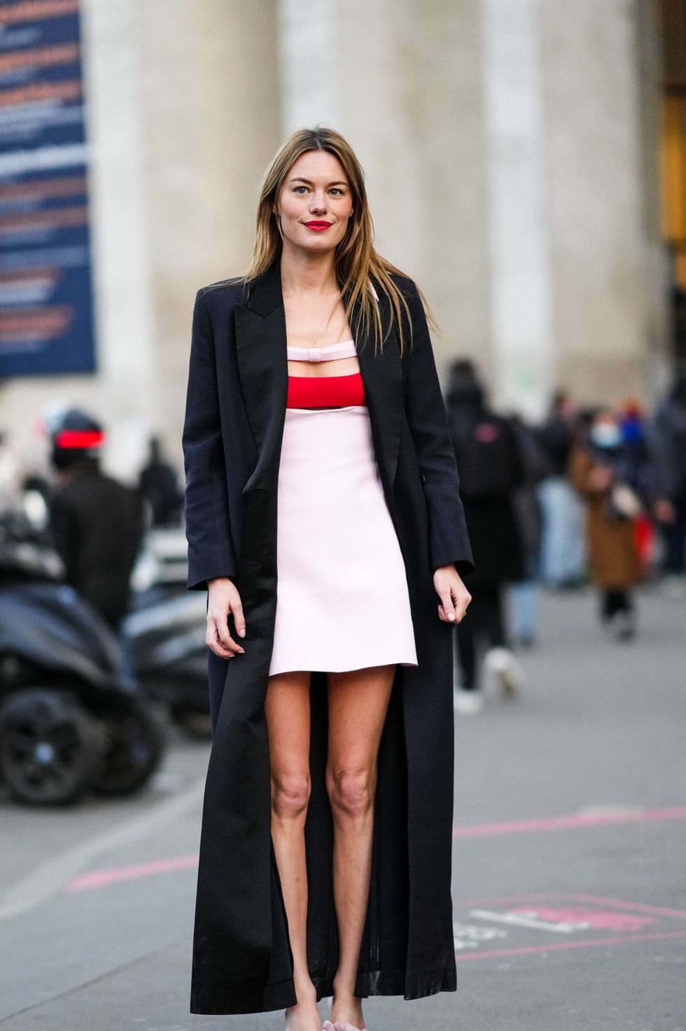 paris, france   march 07 camille rowe wears a white with red strap cut out chest  shoulder off short dress, a black long coat, a gold ring, pale pink shiny leather  puffy knots heels mules  sandals, outside giambattista valli, during paris fashion week   womenswear fw 2022 2023, on march 07, 2022 in paris, france photo by edward berthelotgetty images