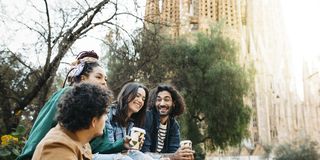 smiling friends taking selfie while sitting on a bench at sagrada familia park, barcelona, catalonia