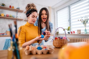 two beautiful young women sitting at home and playing an egg tapping game with easter eggs for easter