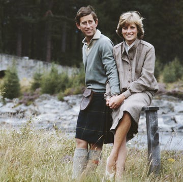 prince charles and princess diana stand in a field near a river and hold hands, both smile