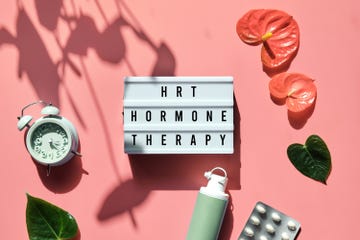 text hrt replacement therapy on light box menopause, hormone therapy concept oestrogen replacement therapy awareness pink background with alarm clock, exotic leaves, pills, estrogene gel