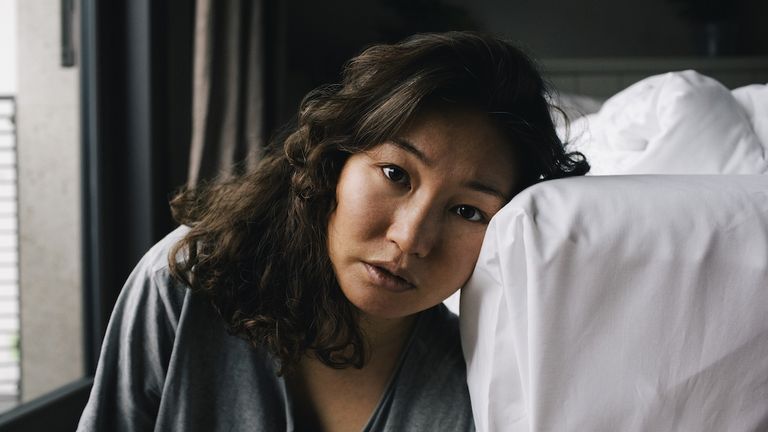 portrait of tired lonely woman leaning on bed at home