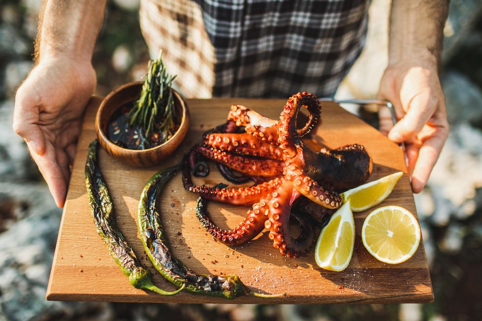 delicious grilled octopus on metal grill seafood bbq with chili sauce, herbs and rosemary octopus with green sweet pepers, chili lemon sauce traditional mediterranean dish or asian cuisine