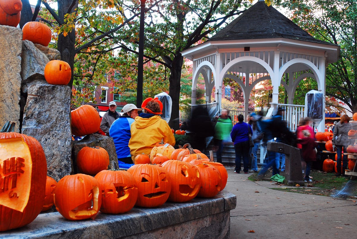 people enjoy the carved pumpkins placed throughout a small public park near halloween in keene, new hampshire