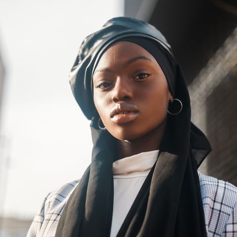 side view low angle of self assured african american muslim lady dressed in stylish checkered blazer with islamic headscarf and leather beret looking at camera with confidence
