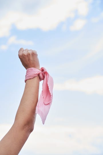 close up shot of a female cancer patient's hand with a pink scarf tied to her wrist. concept of fighting and beating cancer.