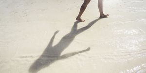 mature woman walking on the beach, on holiday, her shadow prominent in the picture