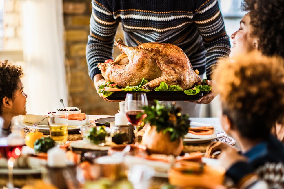 unrecognizable black father carrying thanksgiving turkey while serving it for his family in dining room