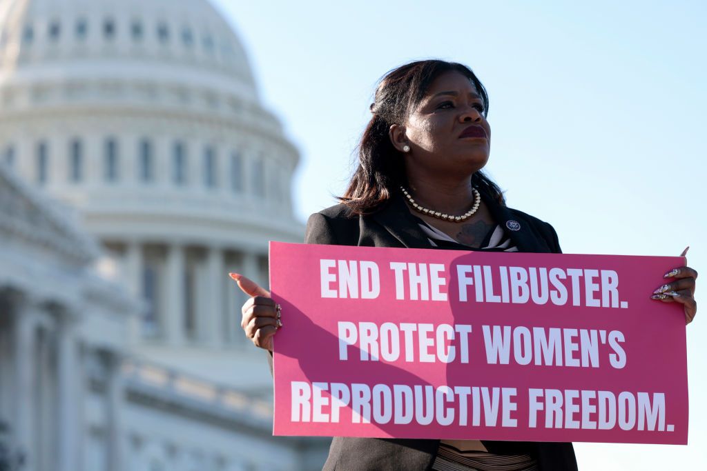 cori bush holding a sign that reads end the filibuster protect women's reproductive freedom