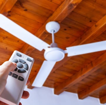 Close up shot of a hand using a remote control to operate a ceiling fan mounted in a house on a wooden ceiling. close up shot of a hand using a remote control to operate a ceiling fan mounted in a house on a wooden ceiling