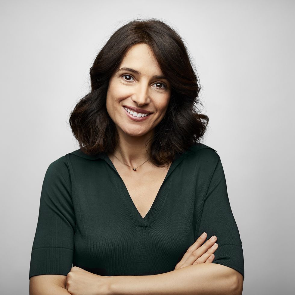 smiling brunette businesswoman standing with arms crossed against gray background confident female professional is wearing green blue top she is having brown hair