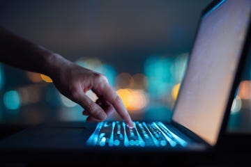 close up of womans hand typing on computer keyboard in the dark against colourful bokeh in background, working late on laptop at home