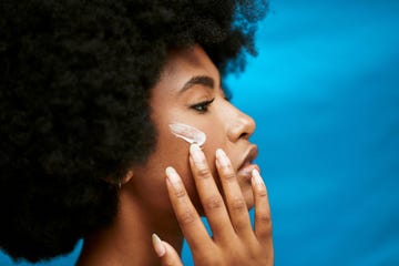 a young african model applying lotion to her skin a closeup of a beautiful nude woman with a dark complexion using a cream for face care in studio against a blue background