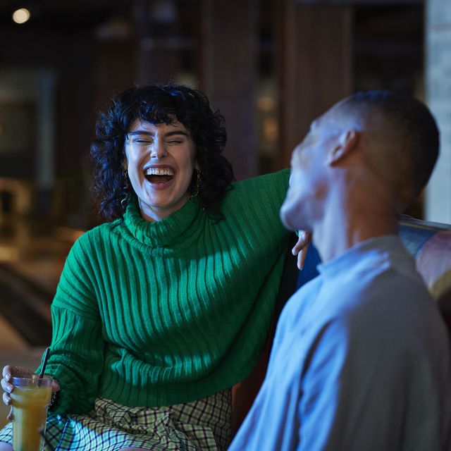 cheerful woman talking while having drink with male friend at bowling alley