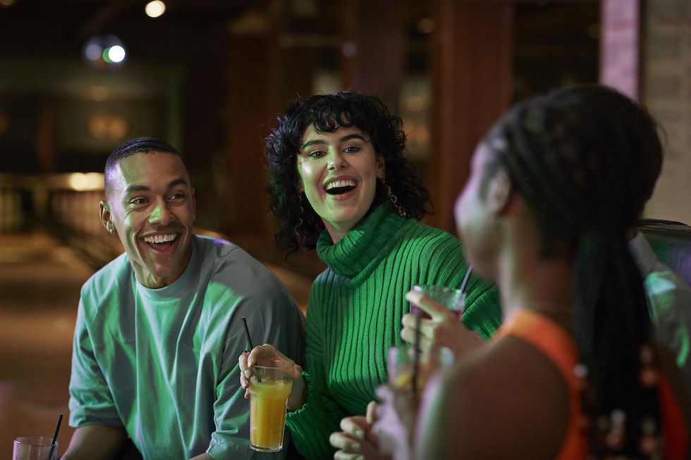 young male and female friends laughing while having drinks together at bowling alley