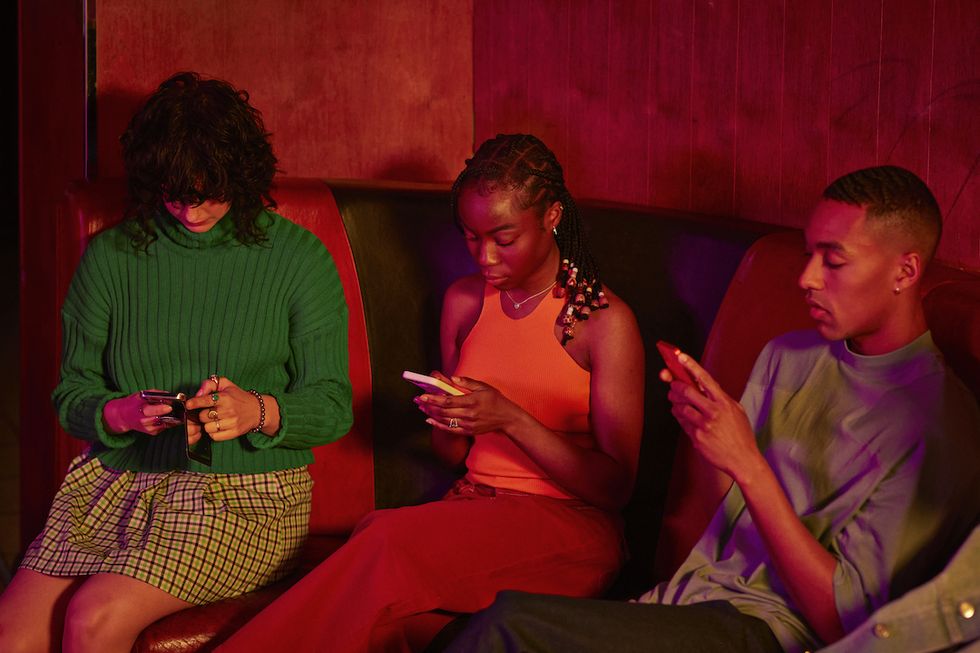 multiracial female and male friends using smart phones sitting on sofa