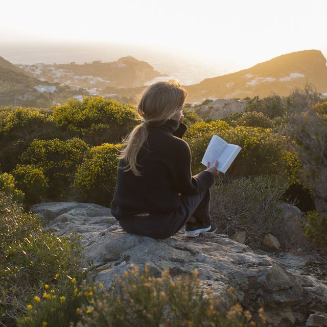 woman sitting on top of a hill, reading a book