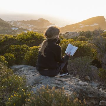 woman sitting on top of a hill, reading a book