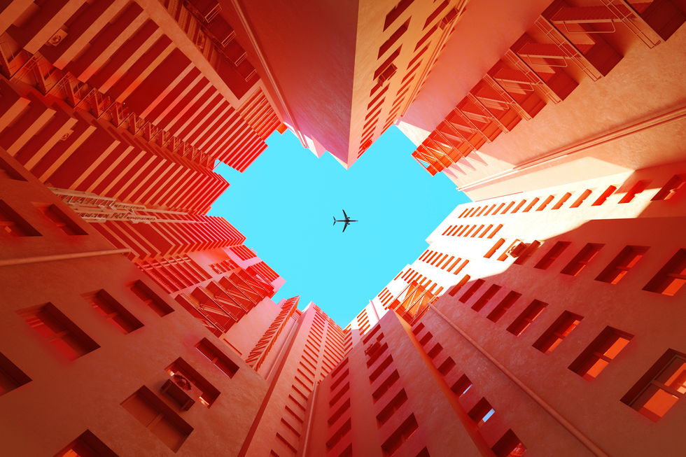 digital generated image of orange buildings making heart shape with airplane flying on blue sky