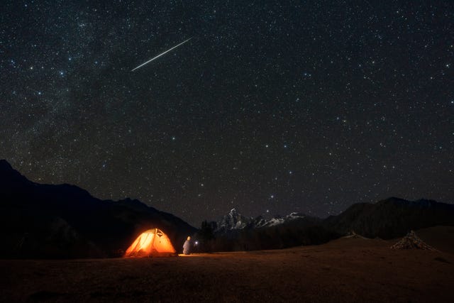 een man kijkt vanaf een camping naar vallende sterren