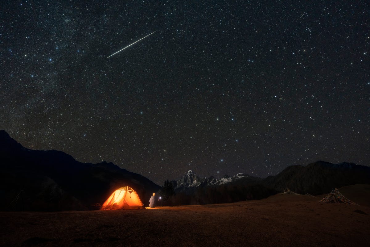een man kijkt vanaf een camping naar vallende sterren