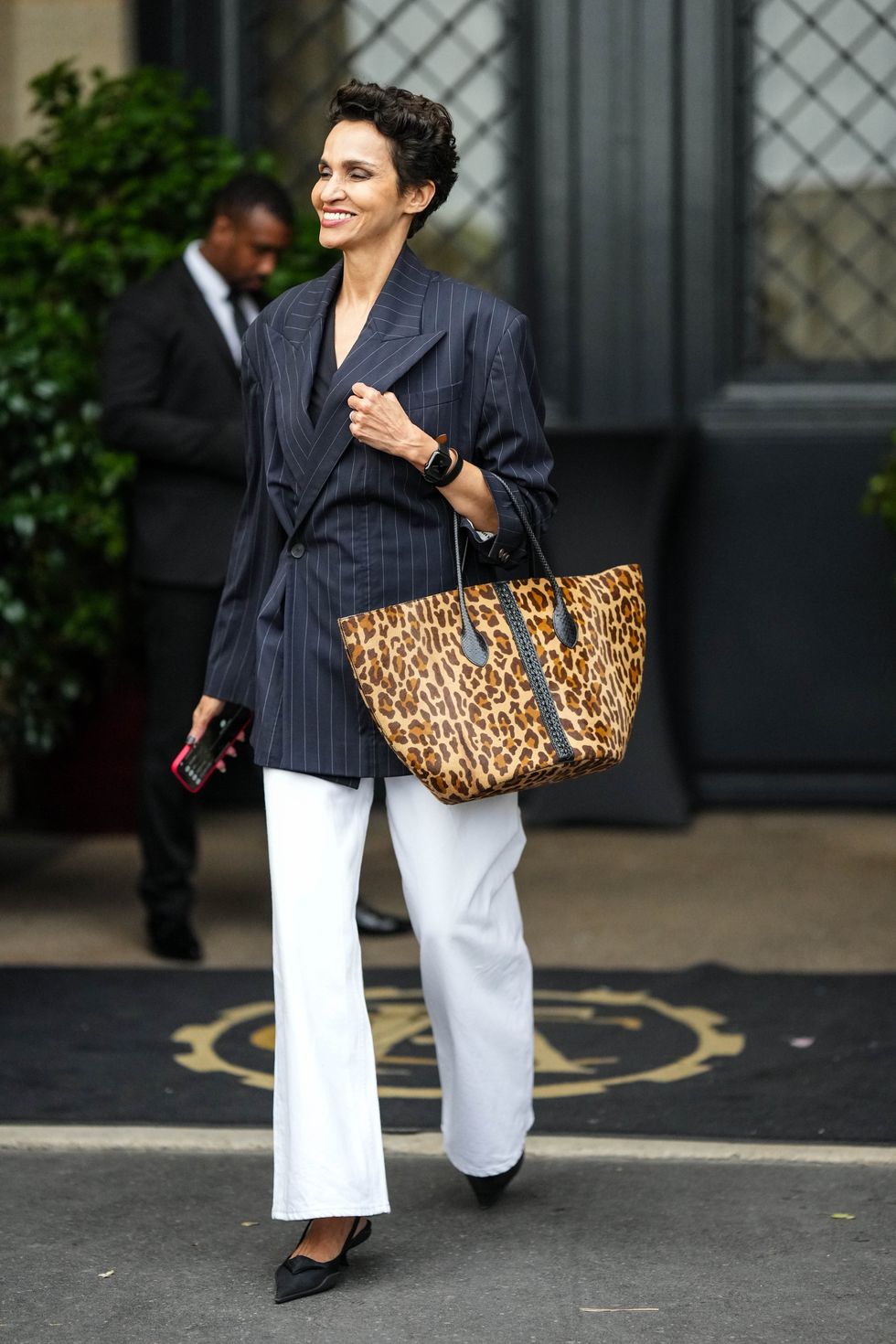 paris, france june 26 farida khelfa wears a black v neck blouse, a black with white small striped print pattern oversized blazer jacket, white denim wide legs pants, a brown and beige leopard print pattern large handbag, black nylon pointed pumps heels shoes from prada, silver rings, a black apple watch, outside the thom browne show, during paris fashion week menswear springsummer 2023, on june 26, 2022 in paris, france photo by edward berthelotgetty images