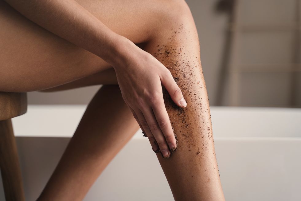 crop shot of woman hand scrubbing legs with organic scrub in bathroom during anti cellulite massage body and skin care peeling and exfoliating procedure