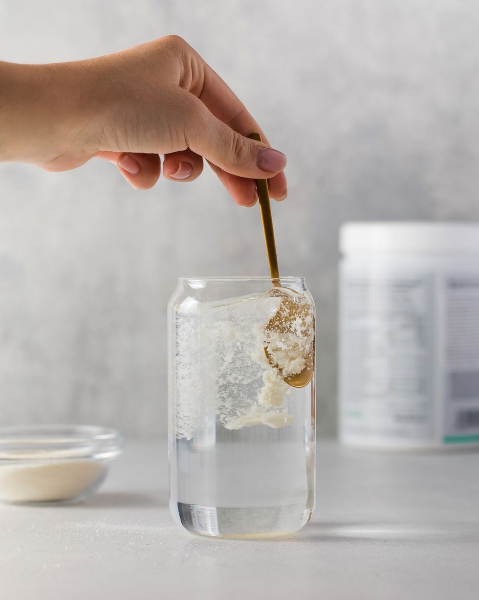 hydrolyzed collagen powder is added with a spoon to a transparent glass of water on a grey background the concept of health, anti aging dietary supplements