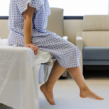 Unrecognizable patient in hospital gown waits for test results an unrecognizable female patient wears a hospital gown and sits on the edge of the hospital bed. she dangles her feet while waiting for her test results.