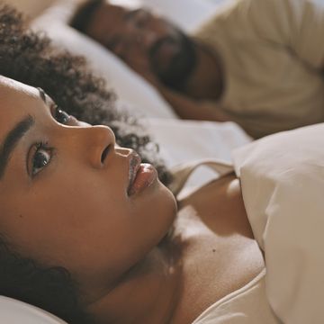 worried female laying in bed with her husband looking anxious and concerned while thinking of her relationship issues a man sleeping while his wife lays awake at night feeling depressed and troubled
