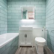 a general interior view of a small bathroom with green rectangular wall tiles, vanity mirror medicine cabinet with led lighting, white bath, square hand basin sink fitted to a vanity cabinet, flush fitting toilet, chrome towel rail radiator and vinyl wood effect floor