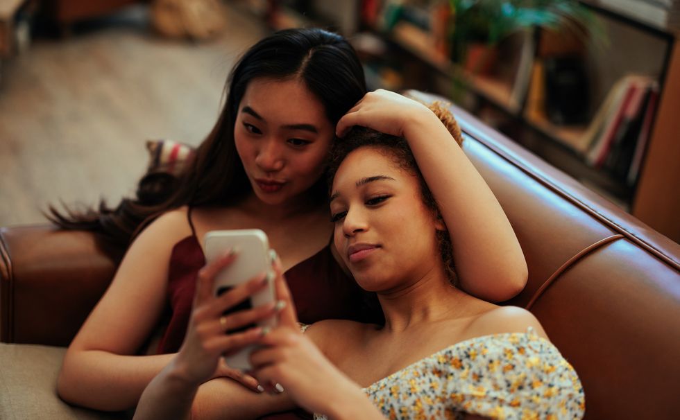 young biracial lesbian women using smart phone while relaxing on a bed