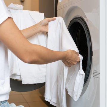 woman loading white color clothes into washing machine in kitchen at home. Close up. Laundry concept. woman loading white color clothes into washing machine in kitchen at home. close up. laundry concept.