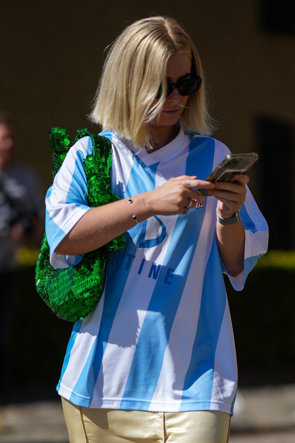 copenhagen, denmark august 10 a guest wears black sunglasses, a white and blue striped print pattern sport oversized t shirt, a green shiny sequined shoulder bag, a pale yellow silk slit split skirt, pink and orange suede sneakers, rings, a watch from apple, outside operasport, during copenhagen fashion week springsummer 2023, on august 10, 2022 in copenhagen, denmark photo by edward berthelotgetty images