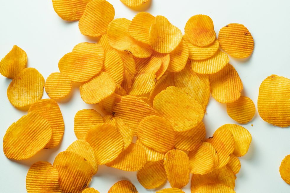crispy fried potato chips are scattered on a white background or table corn spicy fatty chips with paprika and spices the concept of unhealthy diet and lifestyle, accumulation of excess weight copy space background of food